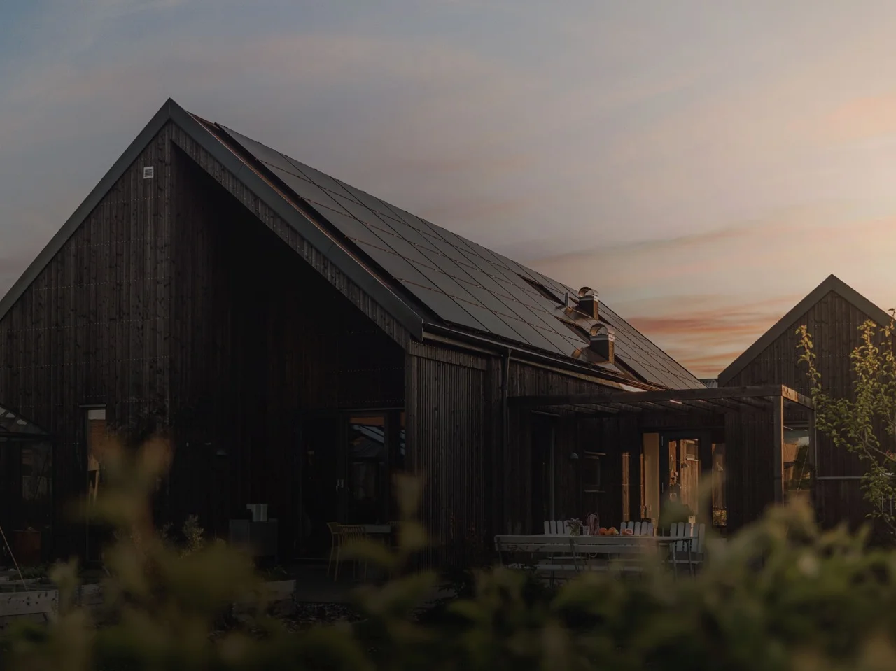 Holzhaus mit Photovoltaikanlage auf dem Dach mit Sonnenuntergang (lohnt sich eine PV-Anlage)