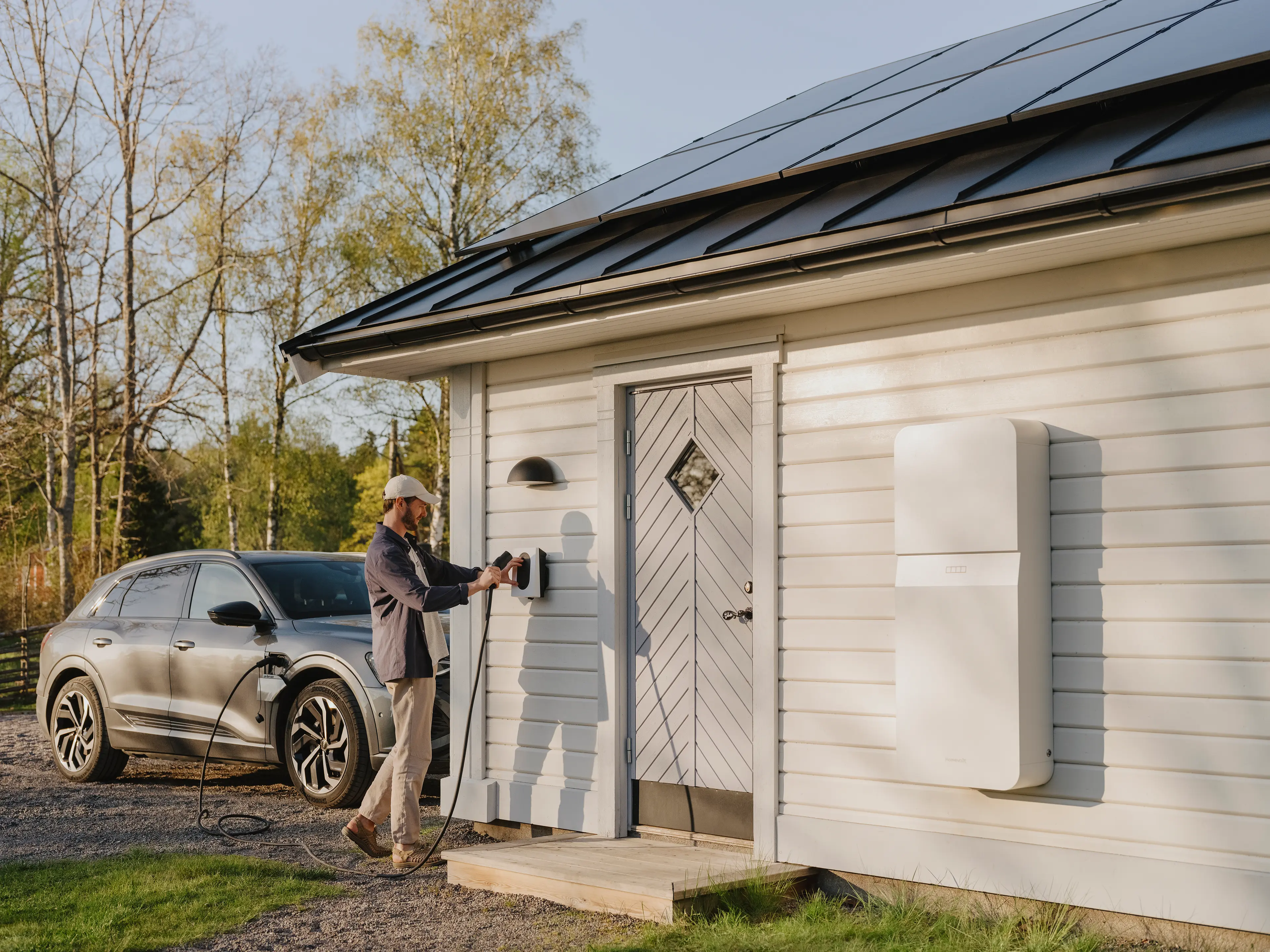 Mann lädt sein E-Auto an der Wallbox. Das Haus hat zusätzlich einen Stromspeicher und eine PV-Anlage.