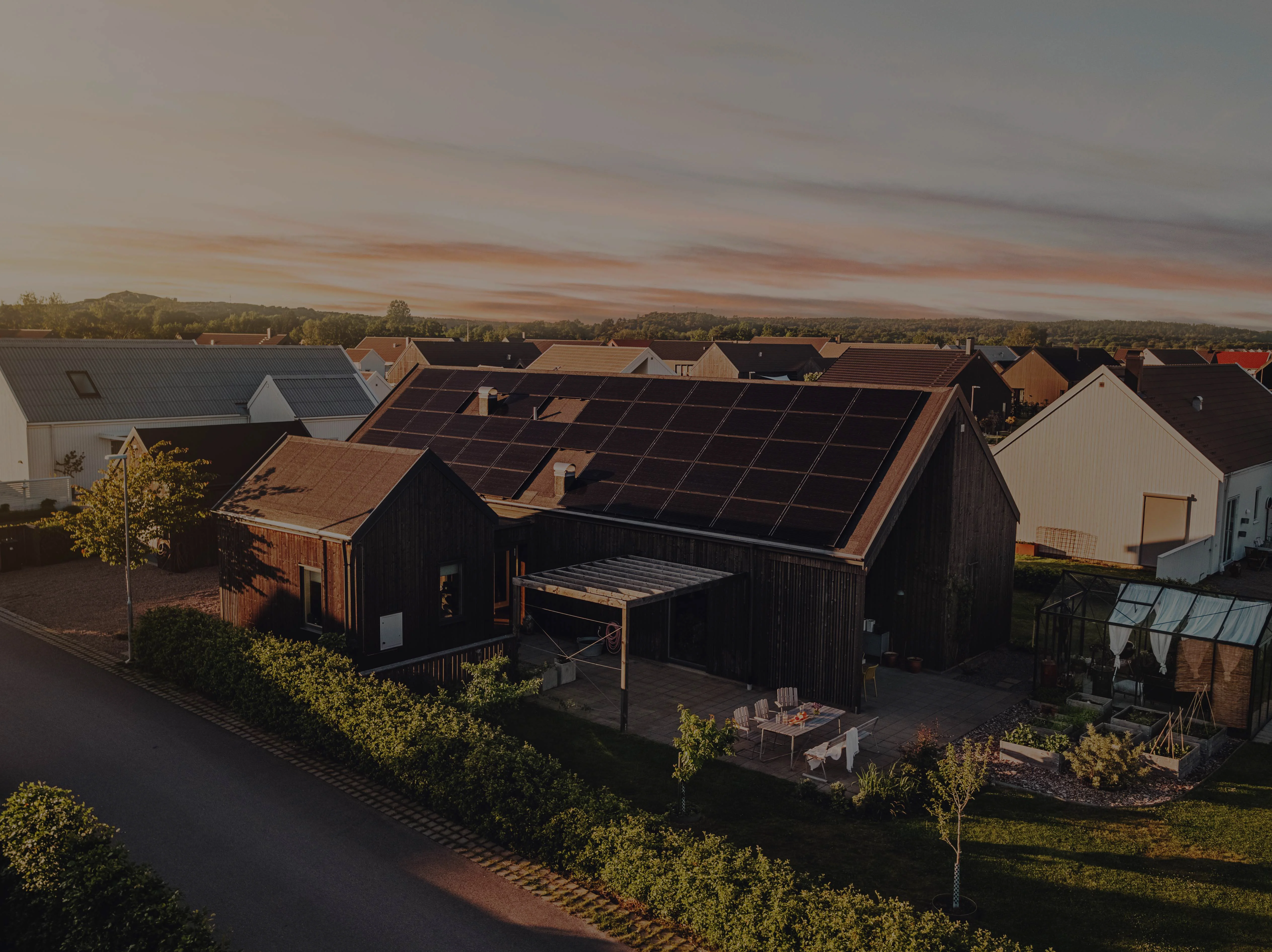 Holzhaus mit Solarpaneelen auf dem Dach. Sonnenuntergang im Hintergrund.